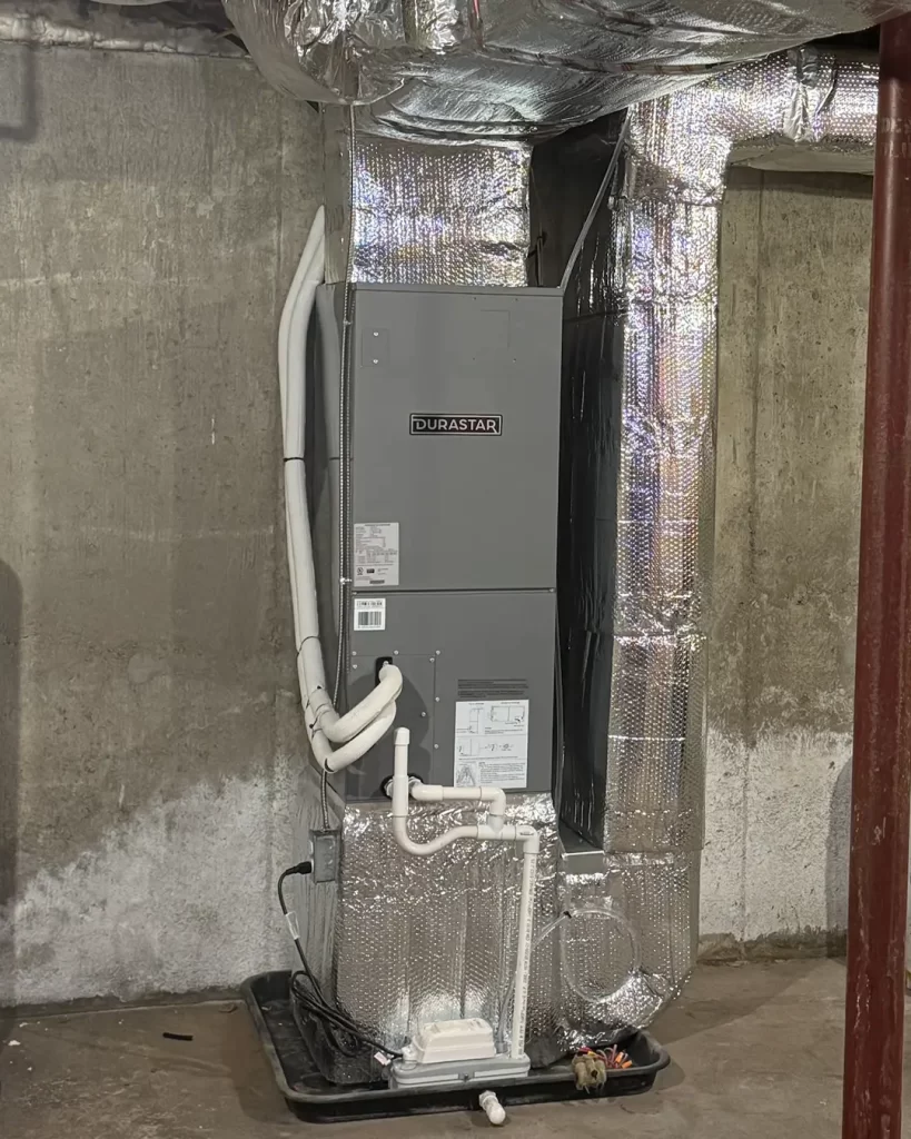 Basement HVAC installation featuring a Durastar air handler connected to insulated ductwork, condensate drain lines, and a safety drain pan, installed against a concrete foundation wall.